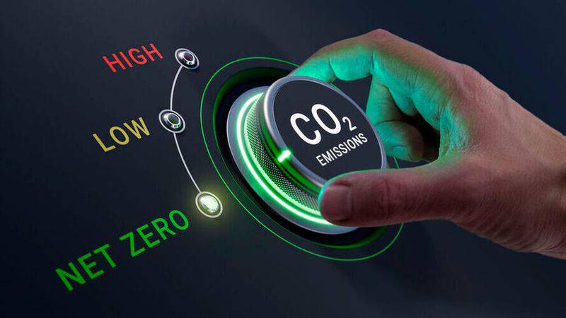 A hand adjusting a futuristic CO2 emissions dial from high to net zero.