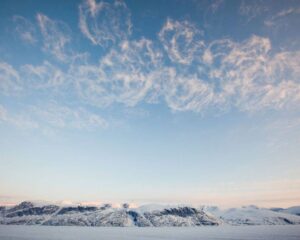 Snow-covered mountains under a sky with wispy clouds at dawn.