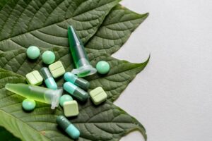 Various pills and a syringe on a large green leaf against a white background.