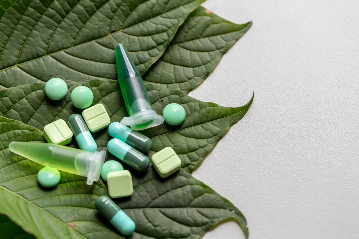 Various pills and a syringe on a large green leaf against a white background.
