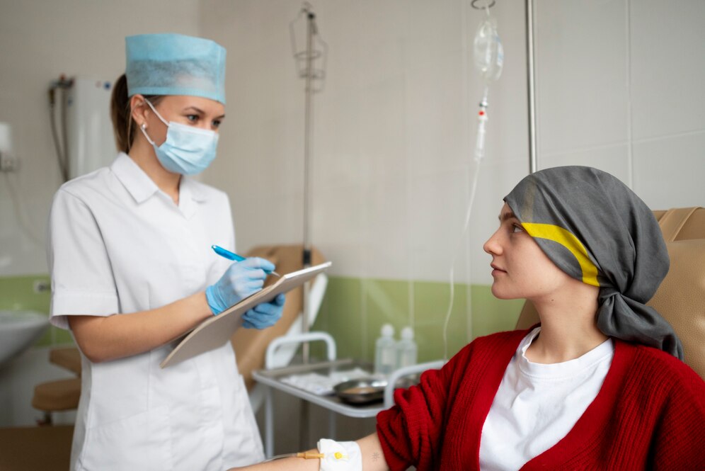 Nurse in mask and cap consulting a patient wearing a headscarf in a hospital room.