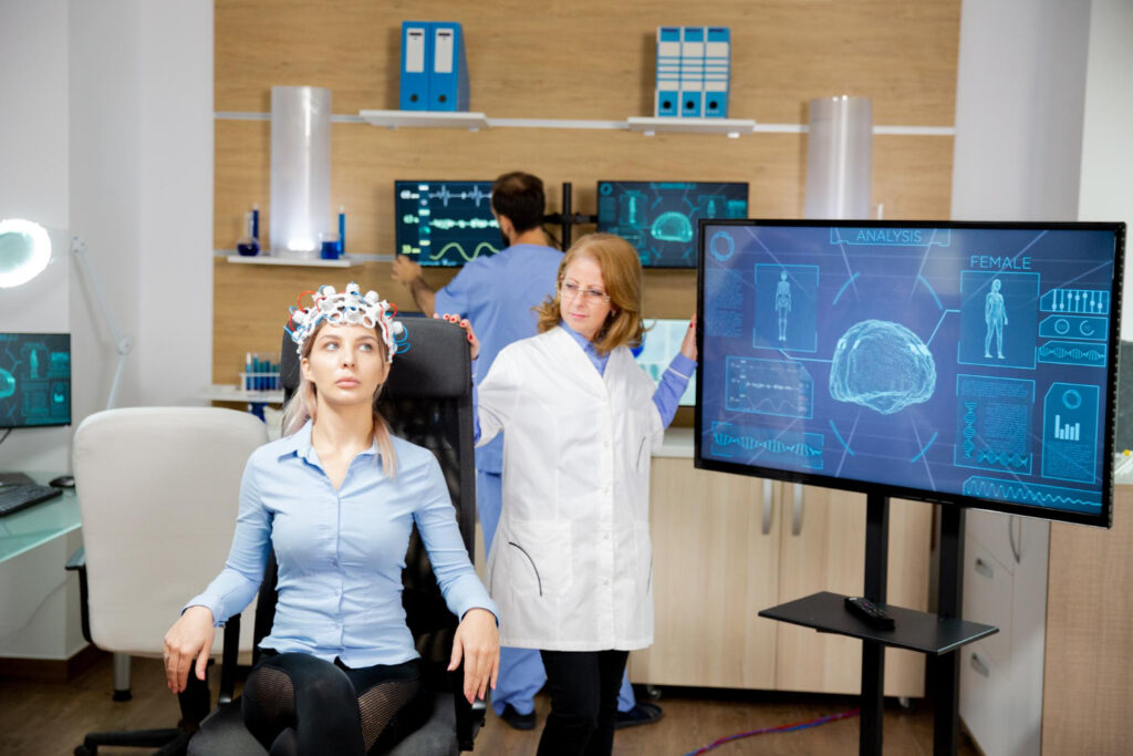 A woman participates in a brain scan study in a lab, monitored by a female scientist using advanced digital analysis screens.