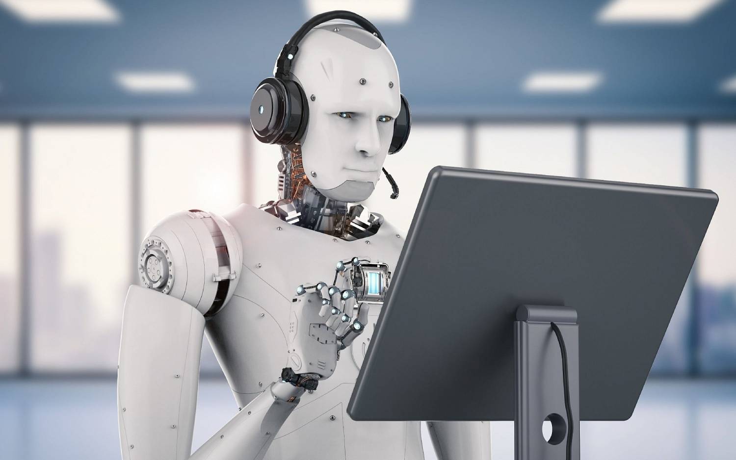 A humanoid robot with headphones using a computer in a modern office setting.