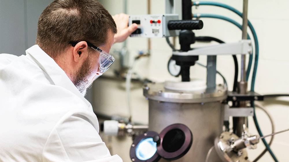 Scientist in lab coat adjusting equipment in a laboratory setting.
