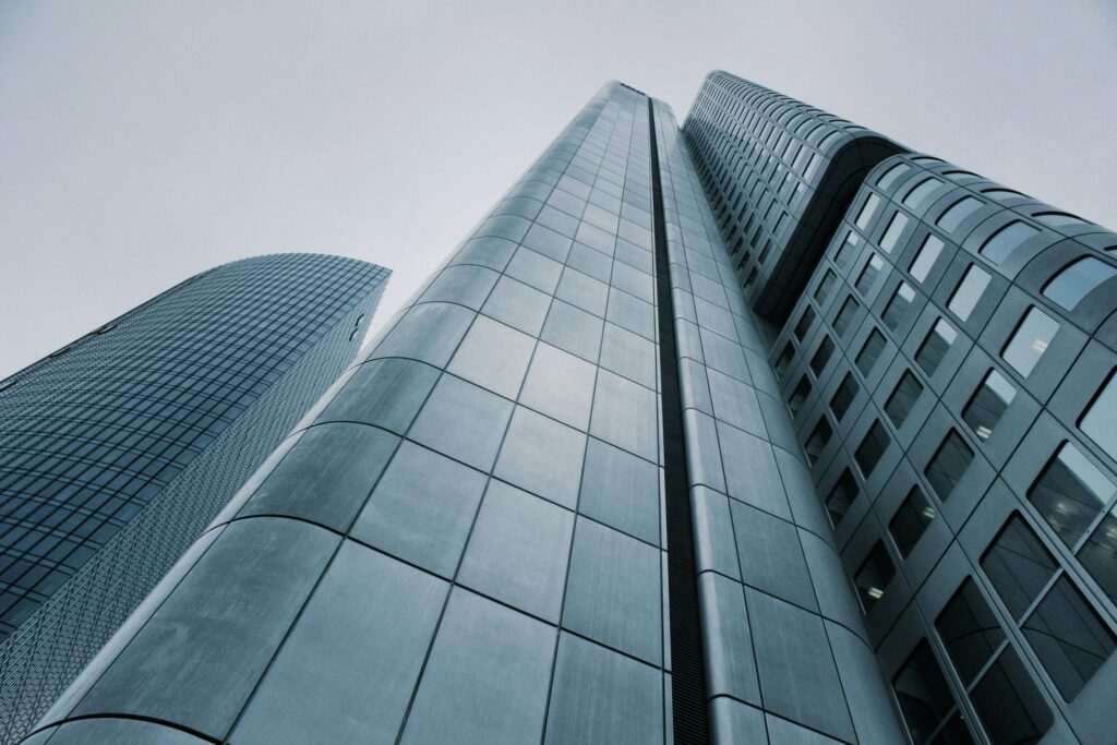 Low-angle view of towering modern skyscrapers with reflective glass facades against a grey sky.