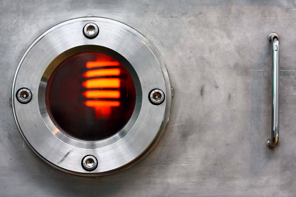 Circular metallic porthole with an illuminated red neon tube on a steel surface.