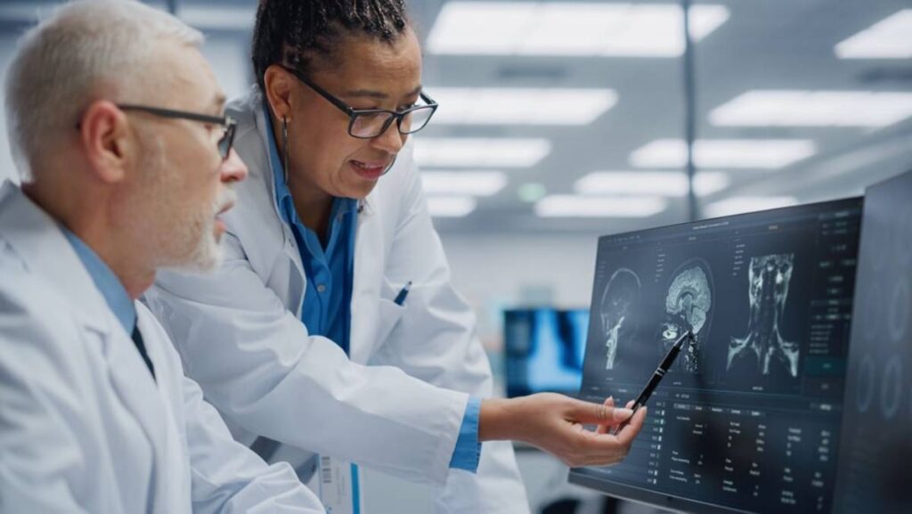 Two medical professionals, a man and a woman, analyzing brain scans on a computer monitor in a laboratory setting.