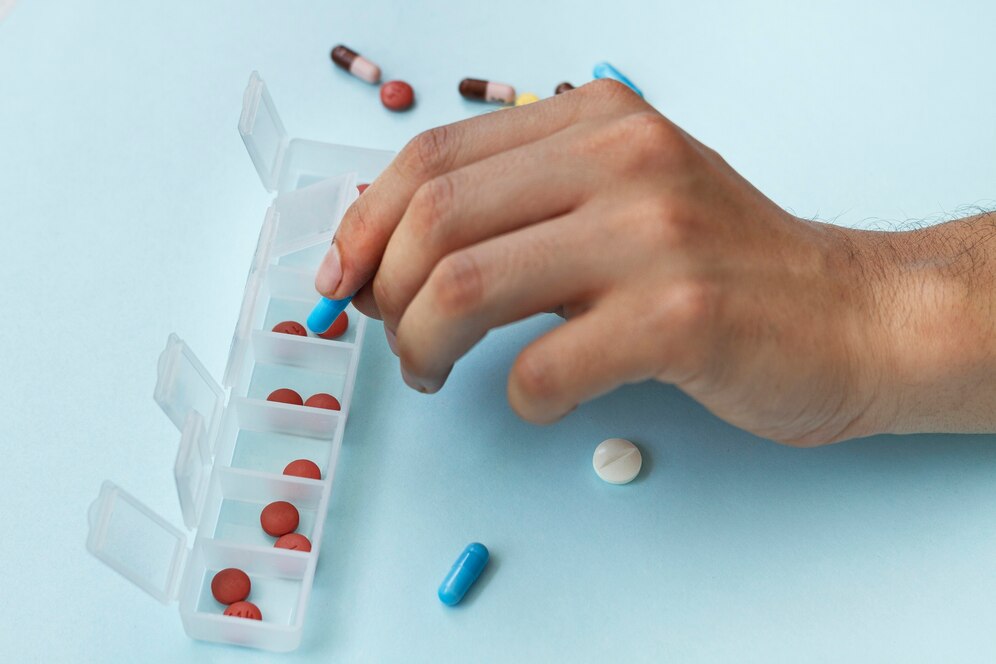 A person organizing pills into a labelled daily pill organizer on a light blue surface.