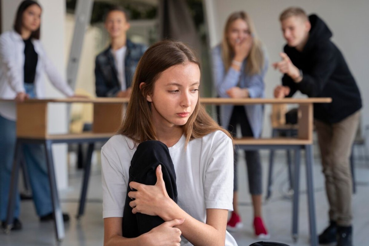 A young girl looks sad as several peers mock her in a school setting.