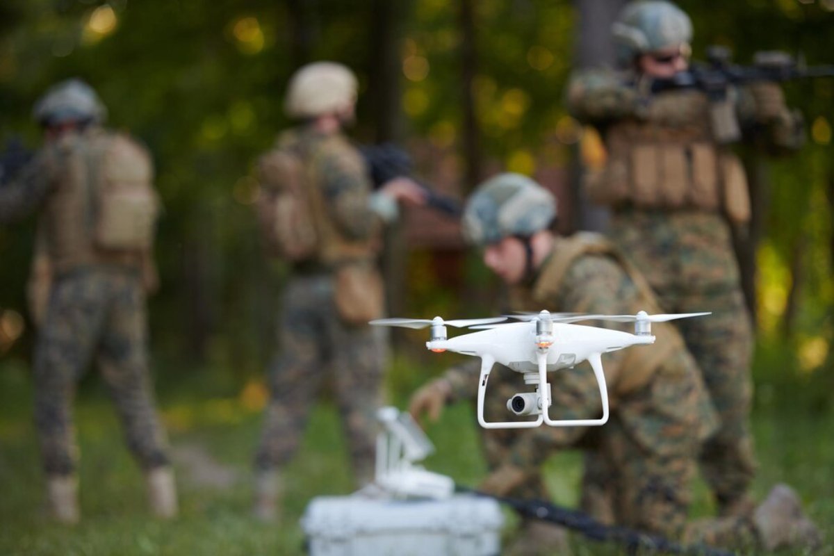 Soldiers in camouflage operate a drone in a forested area during a tactical military exercise.
