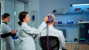 Two female scientists conducting brainwave analysis on a male subject wearing an EEG cap in a laboratory.